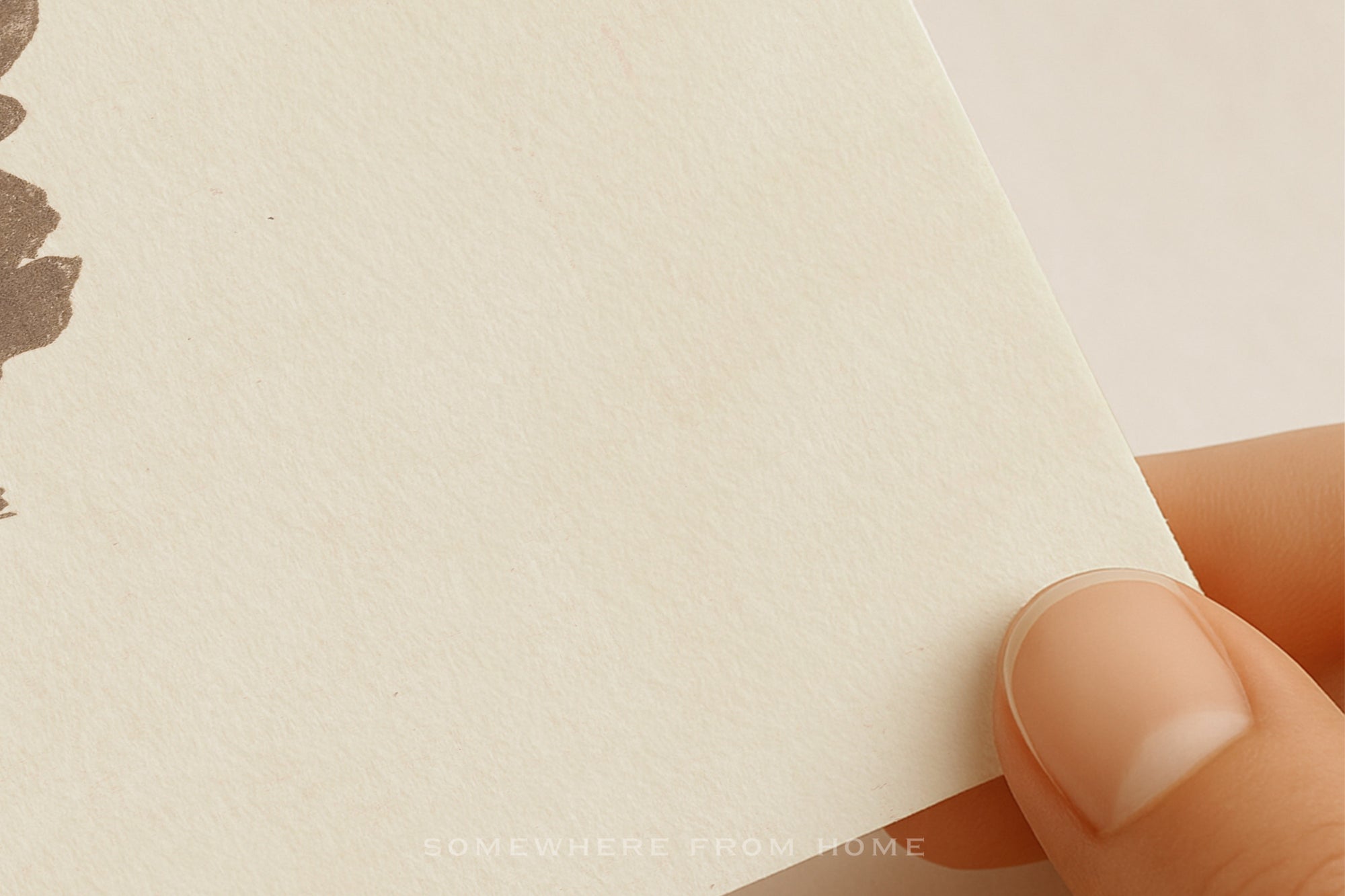 A close-up of a hand holding the corner of a textured off-white paper card or notebook page, with a small brown leaf illustration partially visible on the left side.