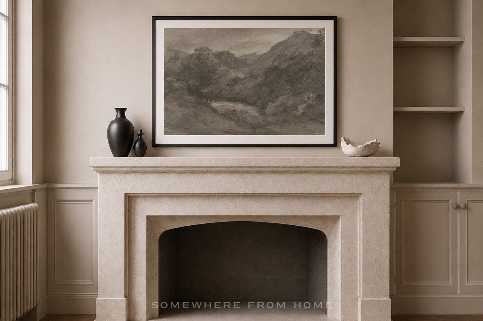 A framed black and white landscape art print hangs on a beige wall above a stone fireplace mantel, styled with a dark vase, a small figurine, and a white bowl. Built-in shelves are visible on the right.