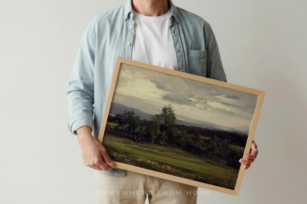 Person holding a framed landscape painting - a moody green landscape painting of a golf course fairway against a plain background