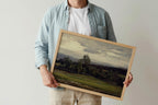 Person holding a framed landscape painting - a moody green landscape painting of a golf course fairway against a plain background