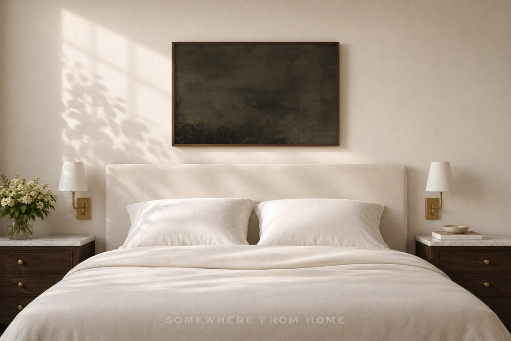 A minimalist bedroom scene featuring a neatly made bed with white linens and pillows, flanked by matching dark wood nightstands with wall-mounted lamps. A large, dark rectangular canvas art piece hangs on the beige wall above the headboard.