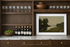Wine bottles on a marble countertop with a framed landscape painting, surrounded by wine glasses and a bowl of limes.