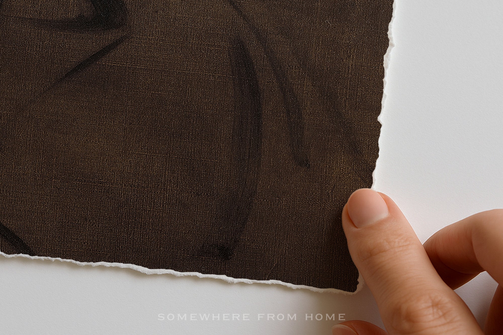 A close-up of a dark brown textured fabric with irregular white tattered edges, held by a person's fingers against a white background. A faint watermark at the bottom reads 'SOMEWHERE FROM HOME'.