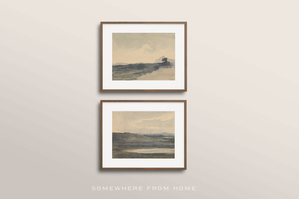 Two framed landscape art prints with white mats and thin brown frames, displayed vertically on a light beige wall. The prints feature soft, muted watercolor-style scenes in gray, blue, and beige tones.