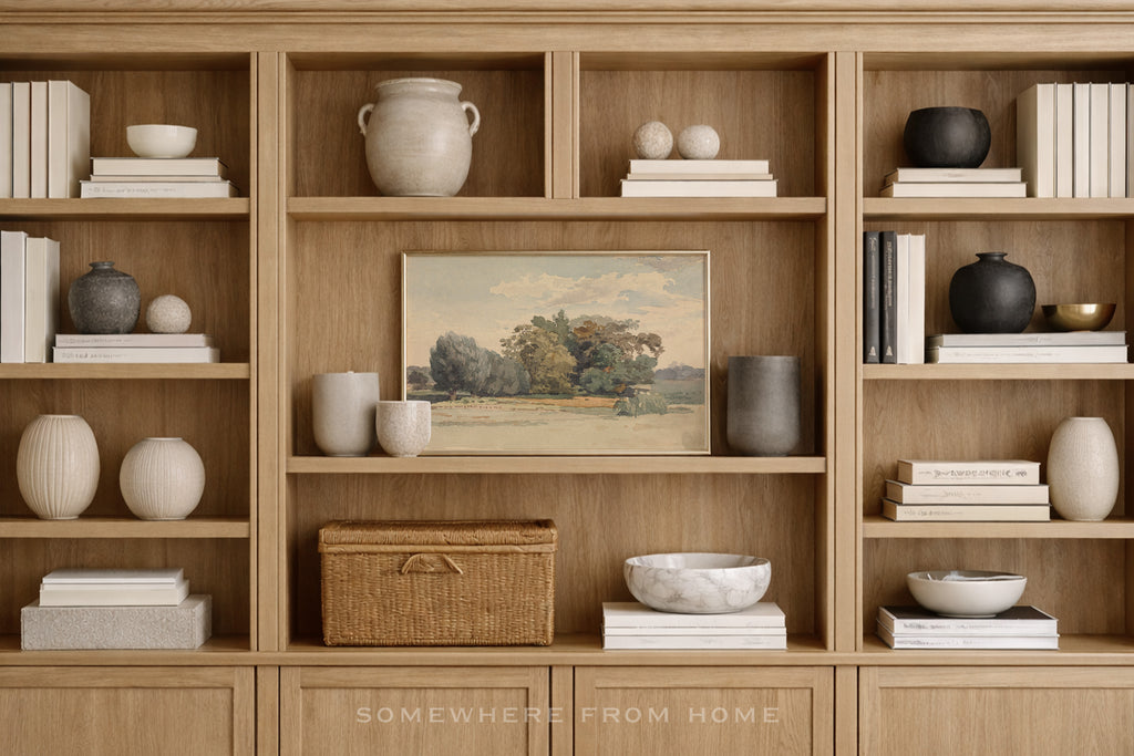 A styled interior scene showing a light wood built-in bookshelf filled with books, ceramic vases, bowls, and a framed landscape painting. The text 'SOMEWHERE FROM HOME' appears at the bottom.