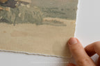 A close-up of a hand holding the edge of a torn paper print featuring a muted landscape in soft green, beige, and gray tones, with a white background and the text 'SOMEWHERE FROM HOME' at the bottom.