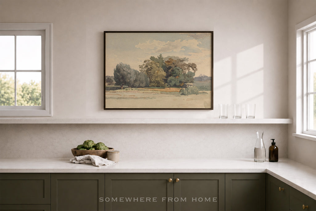 A framed landscape art print hangs on a beige wall above a kitchen counter. The print depicts a tree-lined field under a cloudy sky.