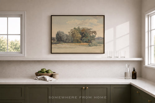 A framed landscape art print hangs on a beige wall above a kitchen counter. The print depicts a tree-lined field under a cloudy sky.