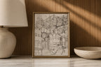 A framed black and white architectural sketch print displayed on a marble surface against a wood-paneled wall, flanked by a lamp on the left and a ceramic bowl on the right.