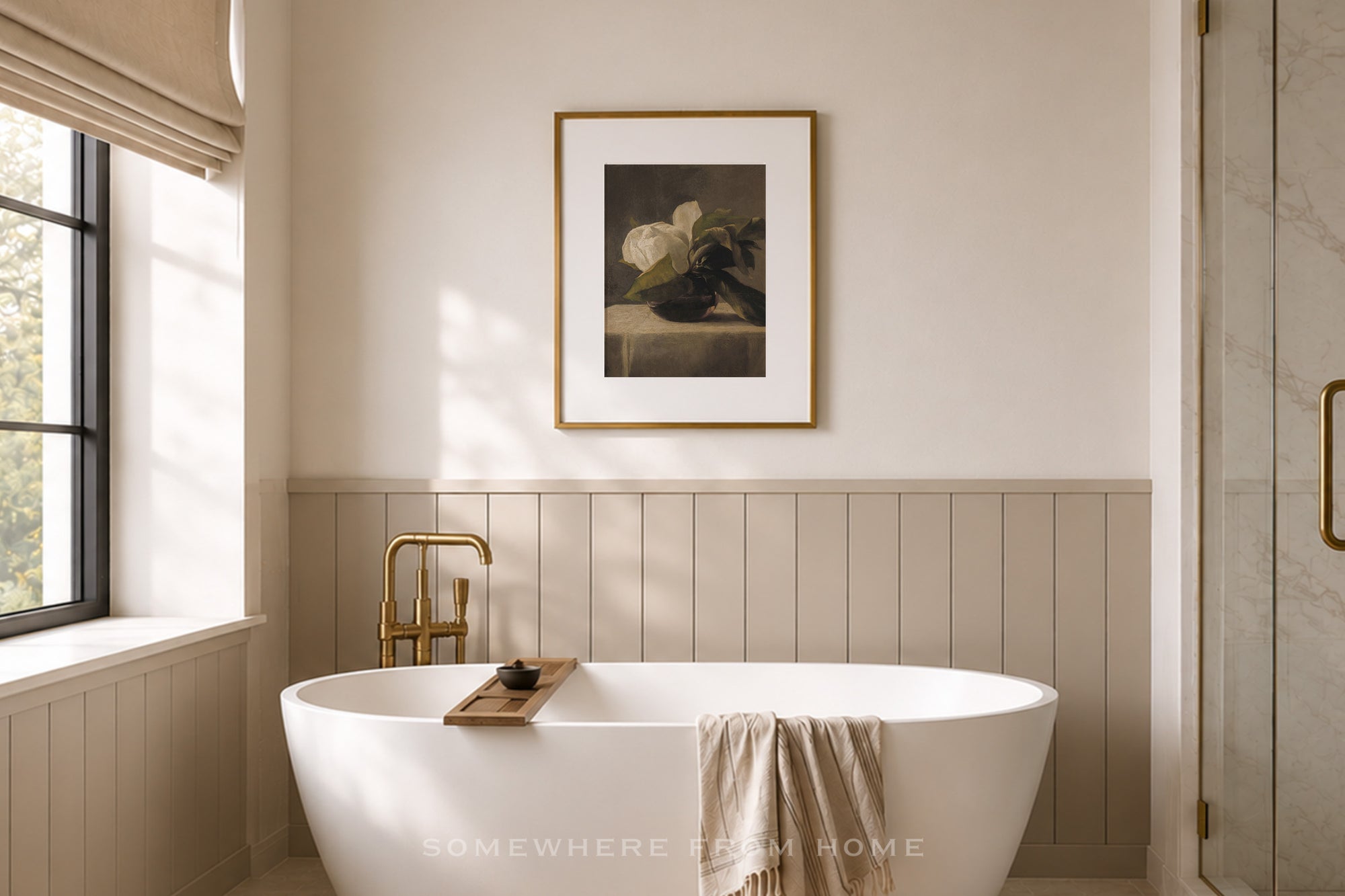 A styled bathroom interior featuring a white freestanding bathtub with a gold faucet, a beige towel draped over the tub edge, a framed still life print on the wall, and a window with a beige blind on the left.