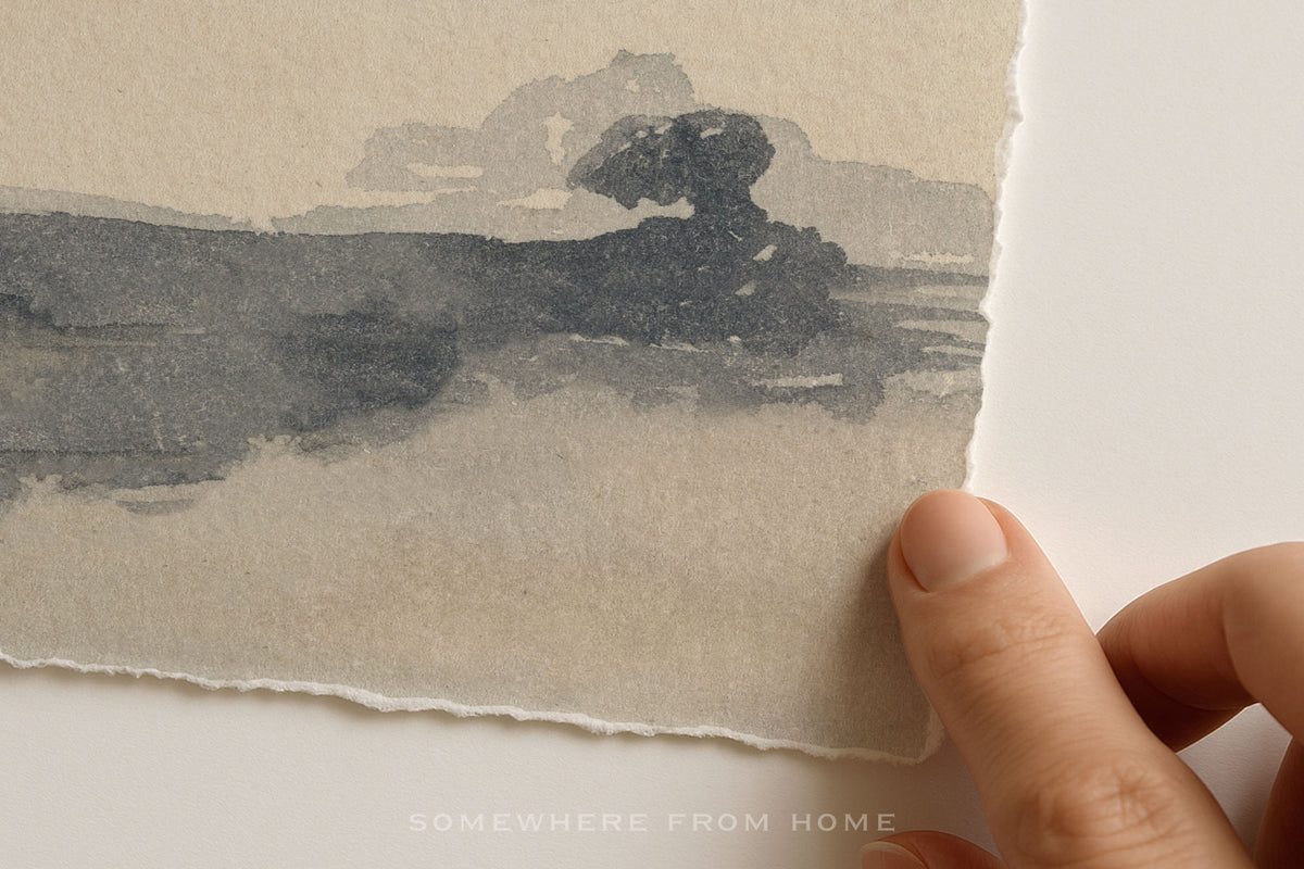 A close-up of a hand holding the edge of a torn sheet of textured paper showing a faint landscape watercolor painting in soft gray and beige tones.