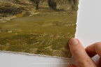 A close-up of a textured oil painting showing brushstrokes of olive green, brown, and gold tones, held by a hand along its torn paper edge against a white background.