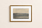 A framed landscape art print with a gold frame and white mat, hanging on a light beige wall. The artwork depicts a muted, minimalist scene of rolling hills under a pale sky.