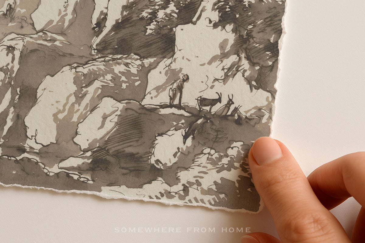 A close-up of a hand holding the edge of a square piece of textured paper featuring a monochrome sketch or print in gray, black, and off-white tones. The hand is visible against a plain light background, and a faint watermark reading 'SOMEWHERE FROM HOME' appears near the bottom.