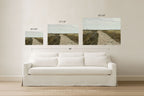 Three framed wall art prints showing a dirt road through a grassy landscape, displayed above a white sofa in a bright room. Size labels for the prints and a total width of 90 inches are overlaid, with the text 'SOMEWHERE FROM HOME' at the bottom.