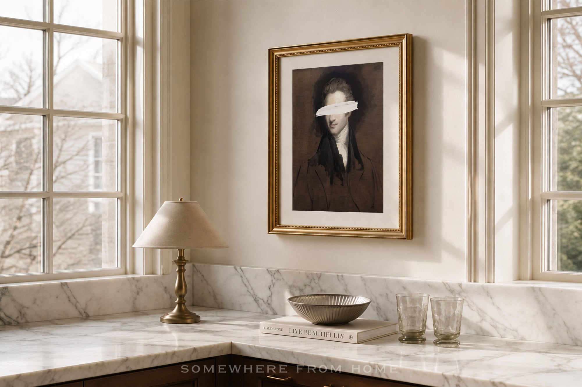 A framed portrait print hangs on a cream wall above a marble countertop in a sunlit room. The artwork shows a dark-haired woman with a white blindfold over her eyes, enclosed in a gold frame.
