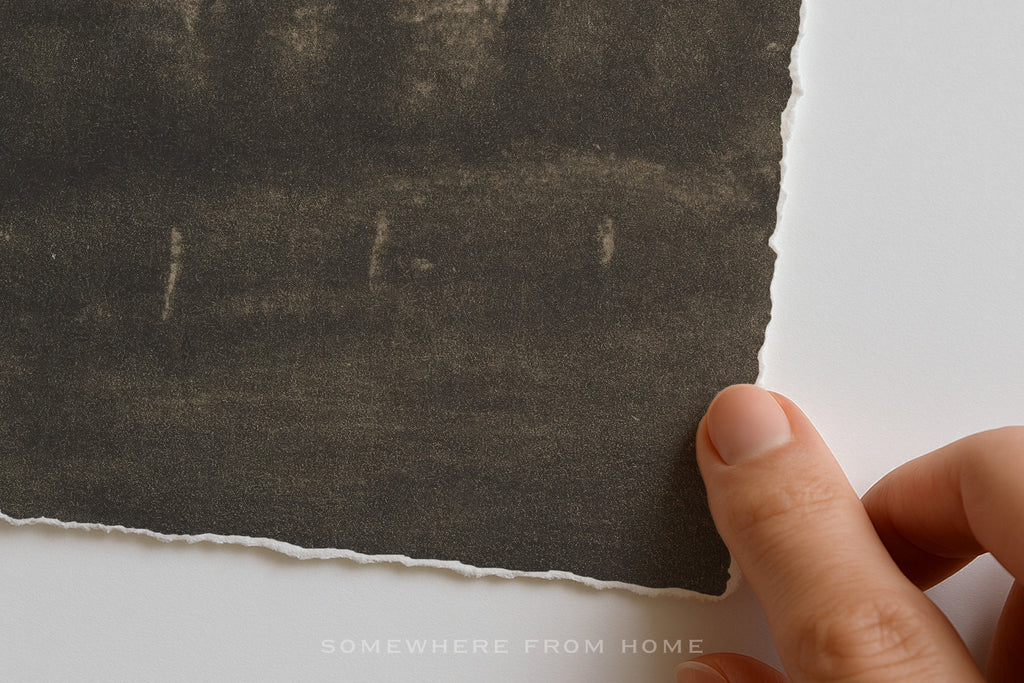 Hand holding a piece of dark textured paper against a white background