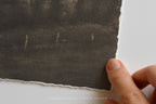 Hand holding a piece of dark textured paper against a white background