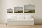 Three framed wall art prints showing coastal dune landscapes in different sizes, displayed above a white sofa in a bright room. Black text above each print indicates dimensions, and a larger 90" width measurement is shown across the set.
