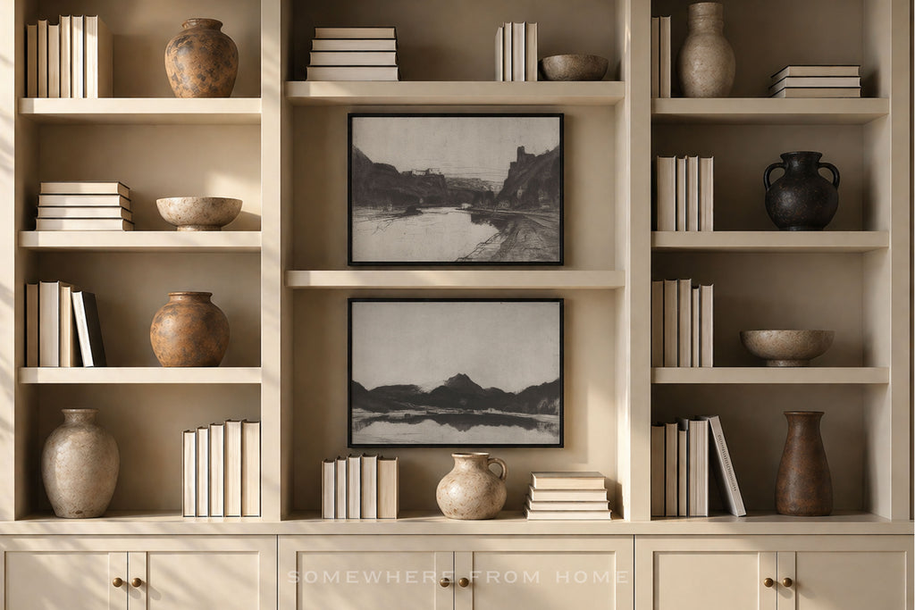 A built-in cream-colored bookshelf with open shelves and lower cabinets, styled with books, ceramic vases, bowls, and two black-and-white landscape framed prints. A watermark reading 'SOMEWHERE FROM HOME' is visible at the bottom.