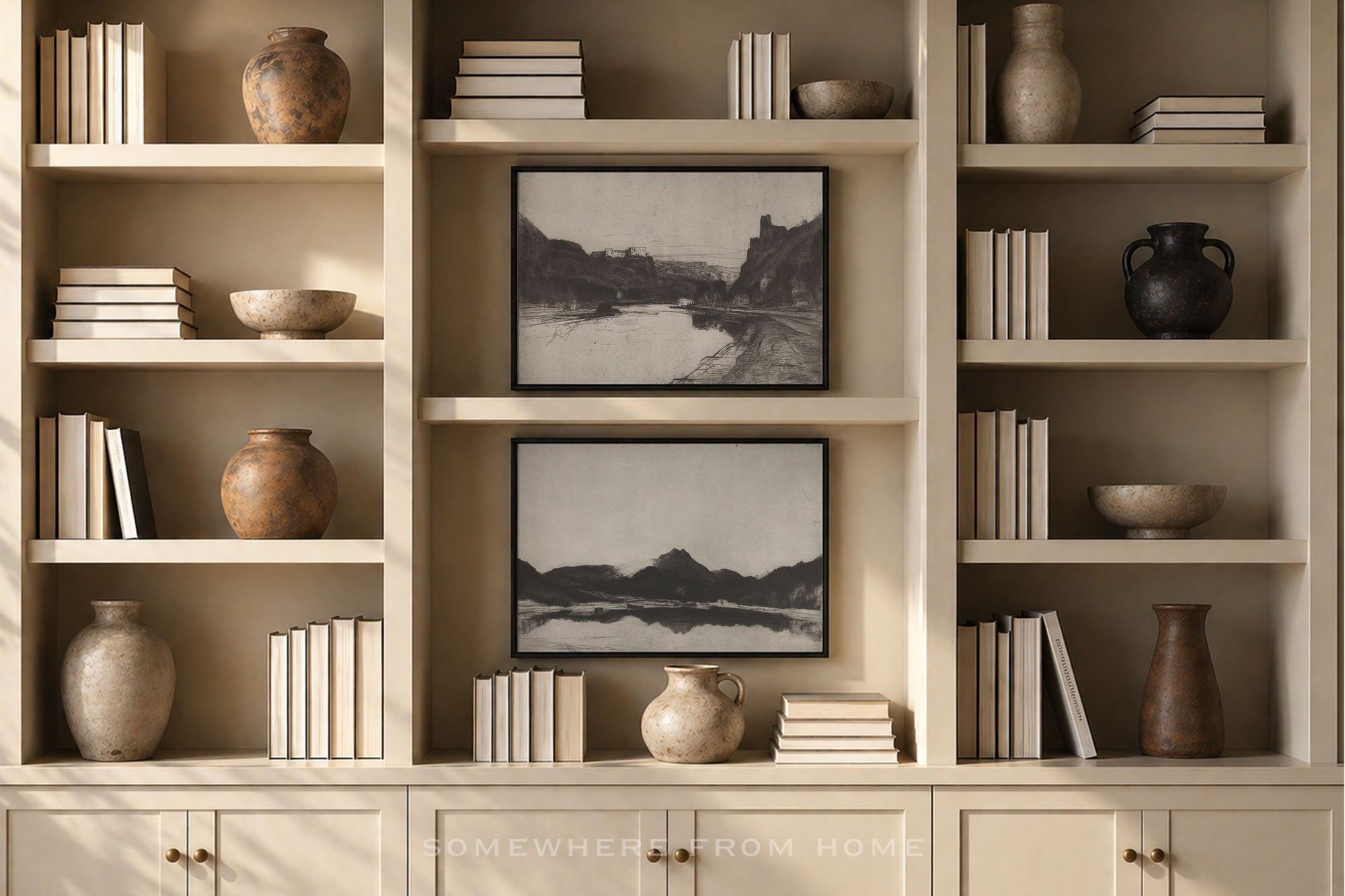 A built-in cream-colored bookshelf with open shelves and lower cabinets, styled with books, ceramic vases, bowls, and two black-and-white landscape framed prints. A watermark reading 'SOMEWHERE FROM HOME' is visible at the bottom.
