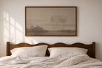 A framed landscape art print featuring two trees in a misty field, hung on a light beige wall above a wooden bed with white striped bedding.