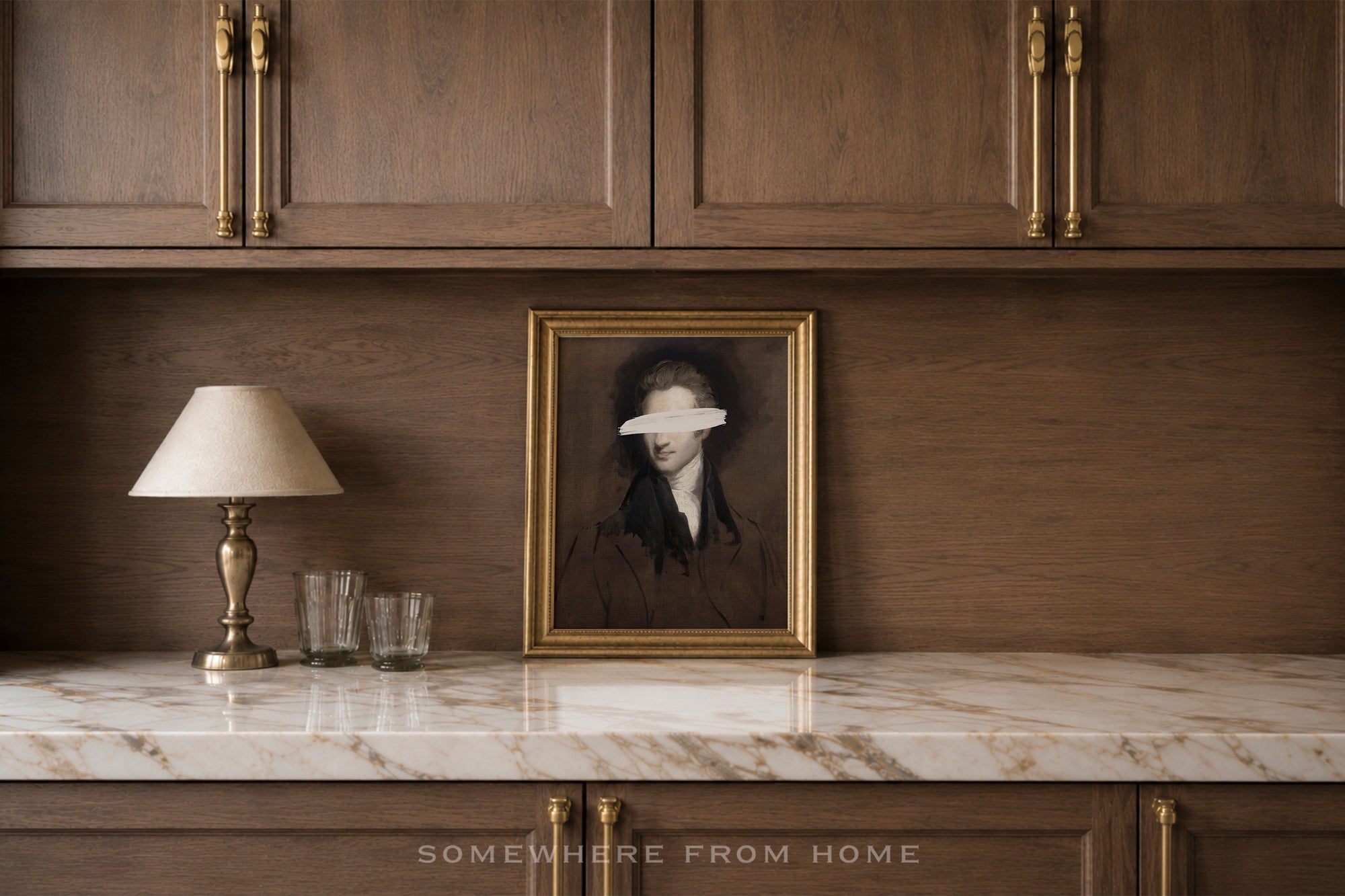 A framed portrait print with a blindfolded figure in dark clothing, displayed on a marble countertop against a dark wood cabinet wall, with a table lamp and two glasses beside it.