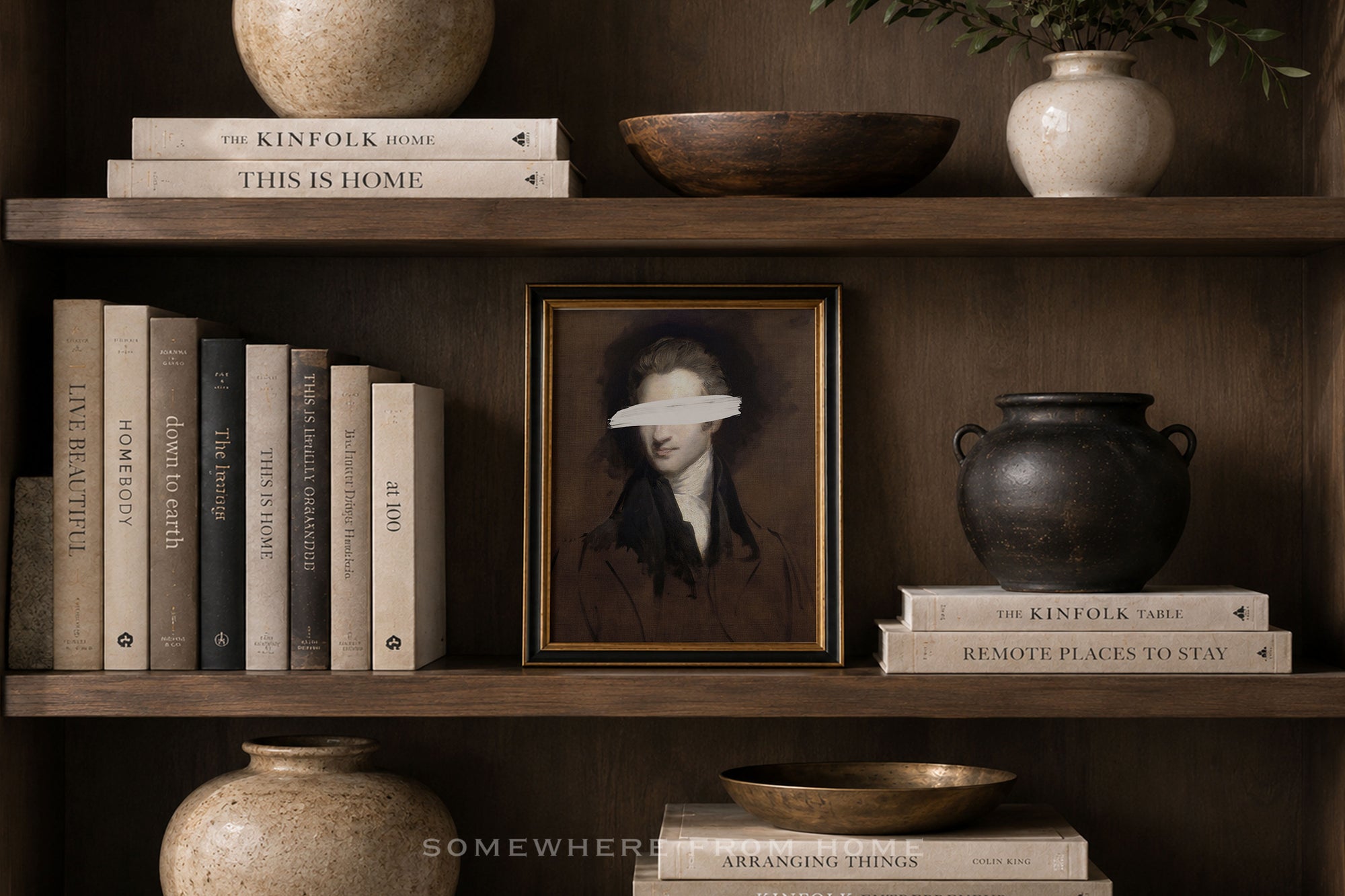 A framed portrait print with a white eye mask over the eyes, displayed on a dark wooden shelf alongside books, ceramic vases, and bowls.