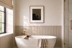 A modern bathroom interior with a freestanding white bathtub, a gold faucet, a framed abstract print on the wall, and a window with a beige blind. The text 'SOMETHING REMEMBER HOME' appears at the bottom.