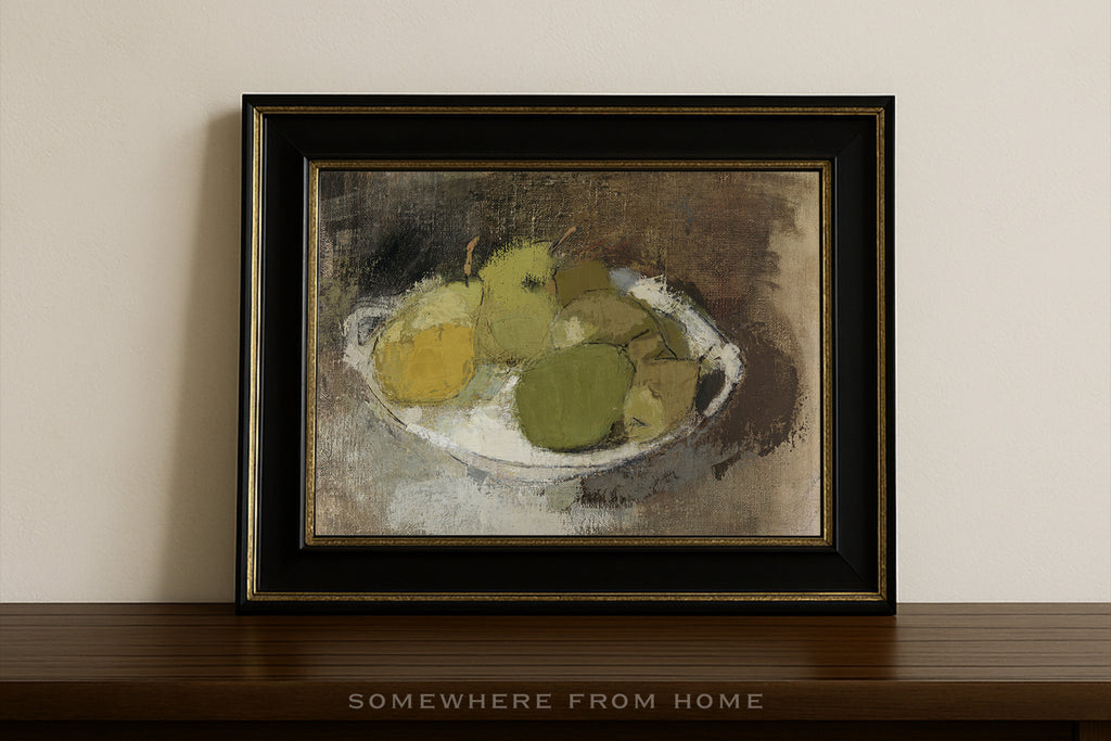 A framed still life painting of green and yellow pears on a white plate, displayed on a dark wooden shelf against a beige wall. The artwork features a black frame with gold inner trim.