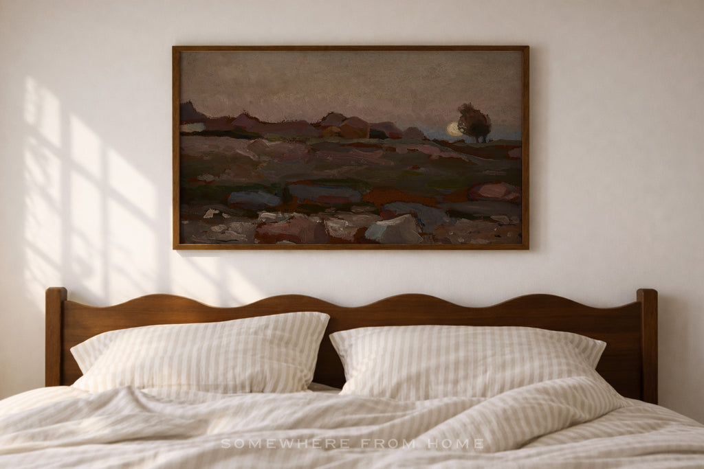 A framed landscape painting hangs on a light beige wall above a wooden bed with white striped bedding. The painting depicts a moody, muted-toned rocky field scene with mountains in the distance.