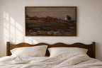 A framed landscape painting hangs on a light beige wall above a wooden bed with white striped bedding. The painting depicts a moody, muted-toned rocky field scene with mountains in the distance.