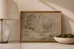 A framed landscape art print with a vintage-style monochrome sketch and a gold frame, styled on a marble surface next to a glass lamp and a bowl of green moss.