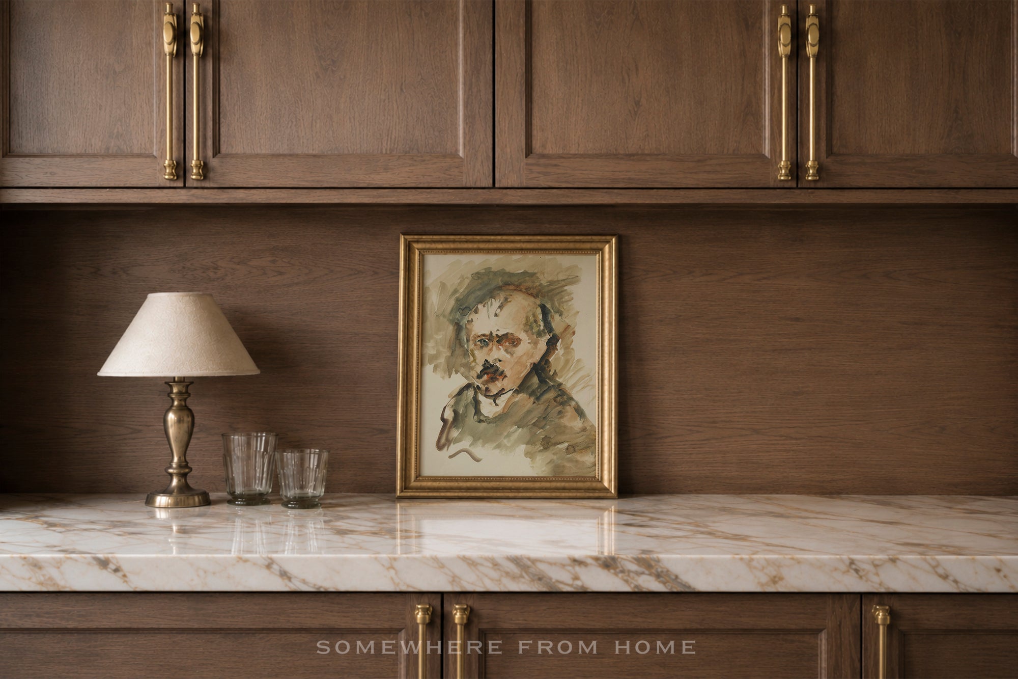 A framed portrait painting of Vincent van Gogh in a gold frame, displayed on a white marble countertop against a dark wood cabinet wall, next to a table lamp and two glasses.