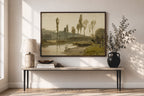 A framed landscape art print hangs on a beige wall above a console table in a styled room. The print depicts a soft, muted countryside scene with trees, a river, and distant hills in beige, green, and brown tones.