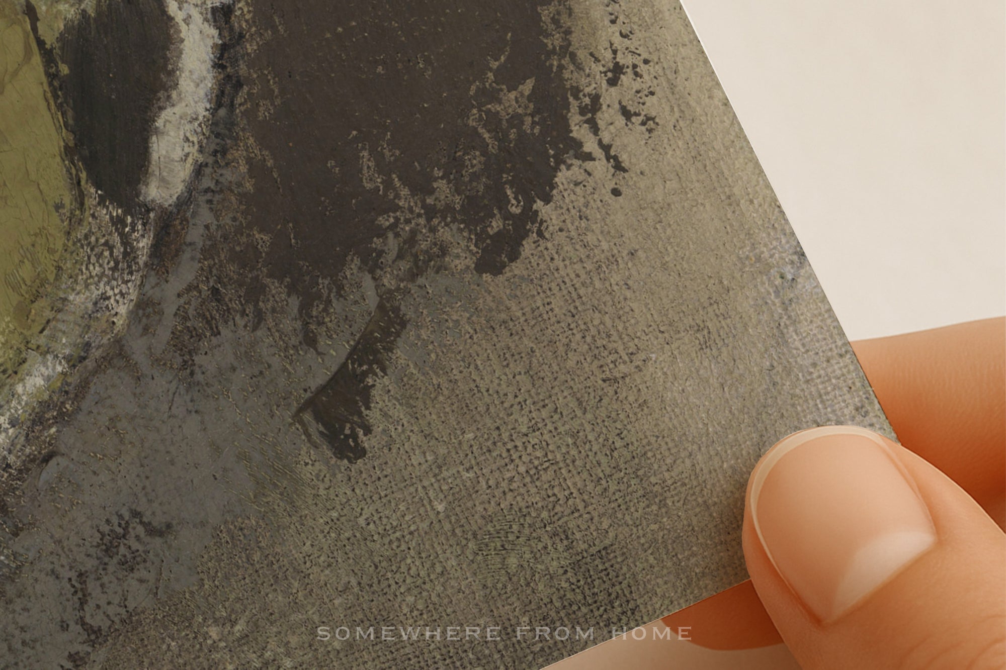 A close-up of a textured fabric or canvas print being held by a hand, showing a dark abstract painted pattern in charcoal, gray, and black tones.