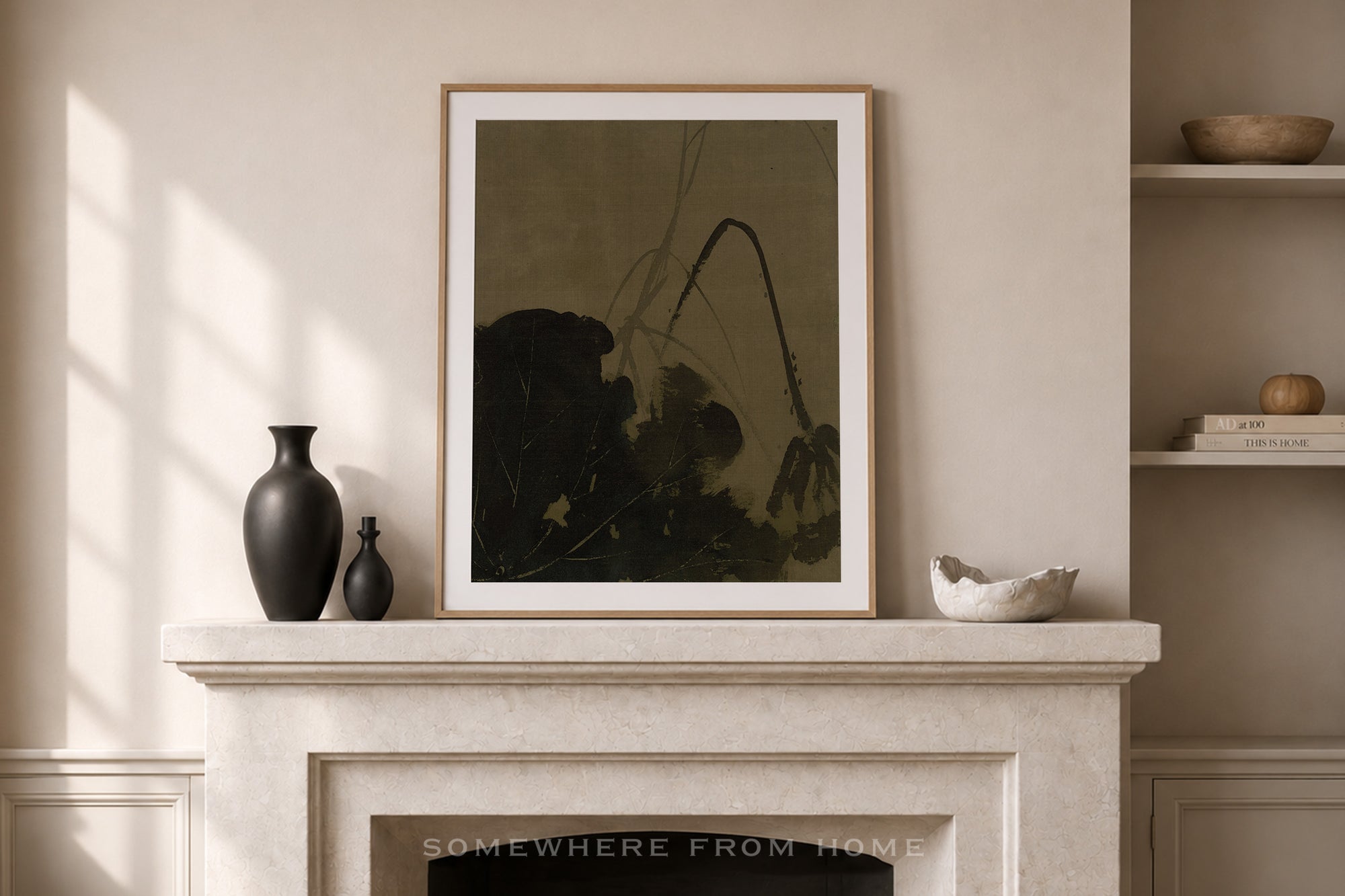 A framed botanical art print with dark olive-green and black tones, displayed on a light stone fireplace mantel in a styled room setting.