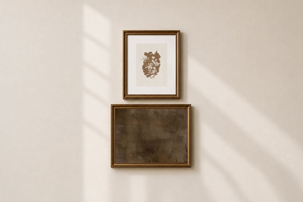 Two framed wall art pieces hanging vertically on a warm beige wall, with soft diagonal sunlight casting shadows across the scene.
