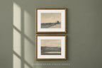 Two framed landscape art prints with gold frames and white mats, hanging vertically on a muted sage green wall with soft window shadow cast across it. The text 'SOMEWHERE FROM HOME' appears below the frames.