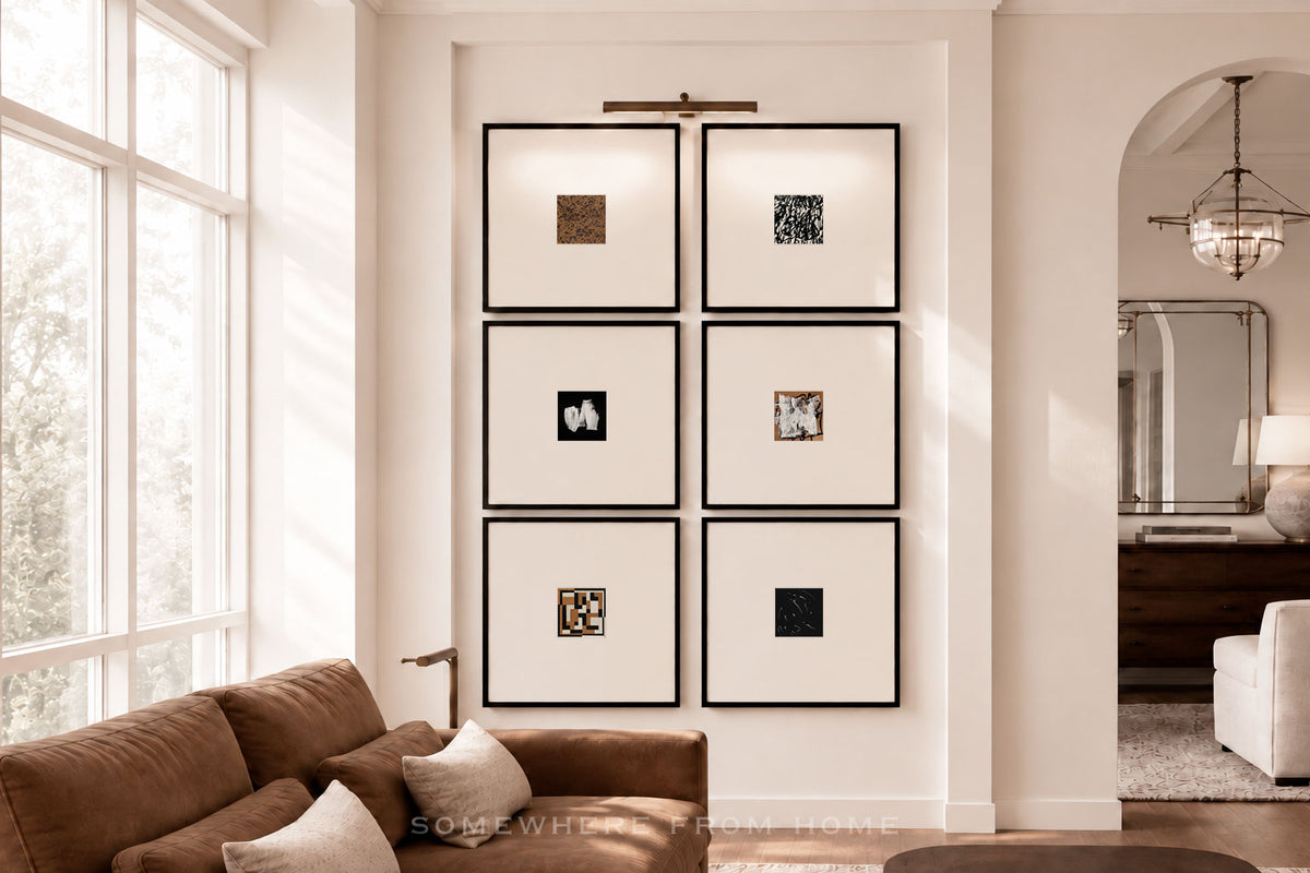 Six framed black and white art prints arranged in a 2x3 grid on a white wall in a bright, modern living room with a brown sofa and large windows.
