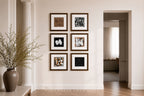 Six framed abstract art prints arranged in a 2x3 grid on a warm beige wall in a styled interior hallway with a white pillar, wooden floor, and a doorway leading to another room.