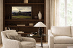 Living room vintage landscape art of golf course with beige sofa, armchair, and wooden bookshelf with TV.
