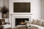 A large rectangular dark brown textured wall art piece hangs above a white marble fireplace in a styled living room with a sofa, striped pillows, and a coffee table.