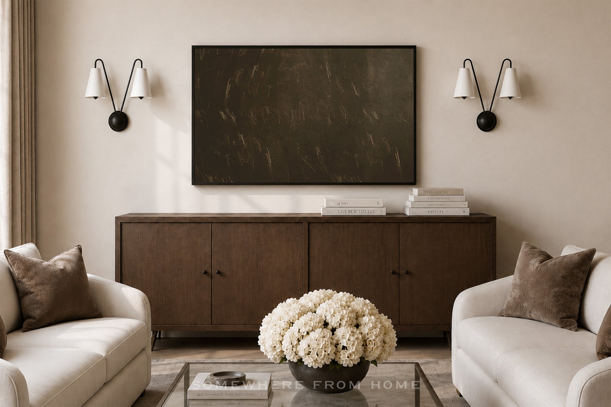 A large rectangular dark brown wall art piece hangs above a wooden sideboard in a styled living room with two cream sofas, wall sconces, and a glass coffee table with white flowers.