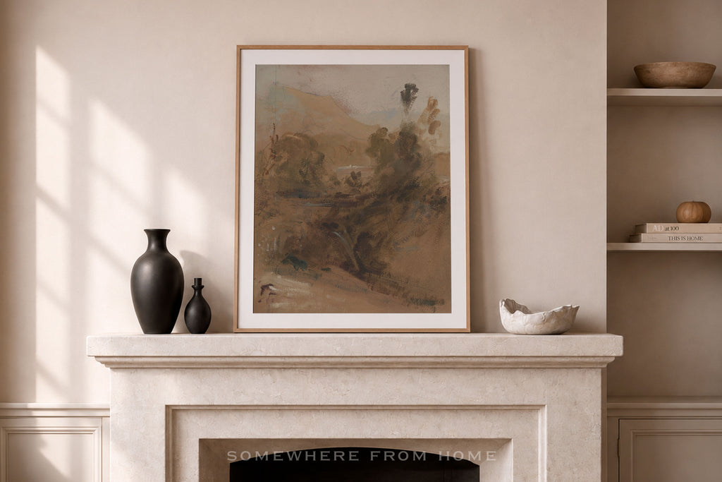 A framed art print depicting a soft-focus landscape in earthy brown and beige tones, styled on a white fireplace mantel in a warm, neutral room with decorative vases and shelves.