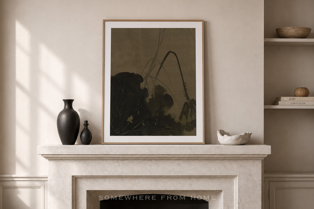 A framed abstract art print with a dark olive-green and black design, displayed on a light beige stone fireplace mantel in a styled room setting.