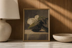 A framed still life painting of white flowers with green leaves in a dark bowl, displayed on a marble surface against a wood-paneled wall with warm sunlight and shadows. A lamp is on the left and a bowl is on the right.