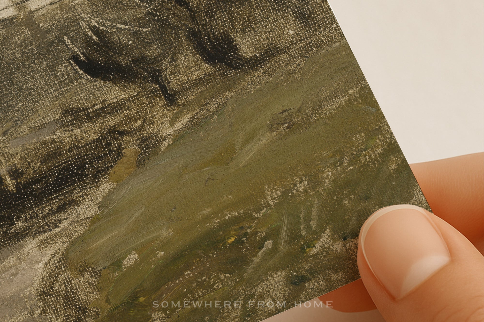 A close-up of a hand holding a small textured painting or canvas showing an abstract landscape in muted olive green, gray, and brown tones against a plain light background.