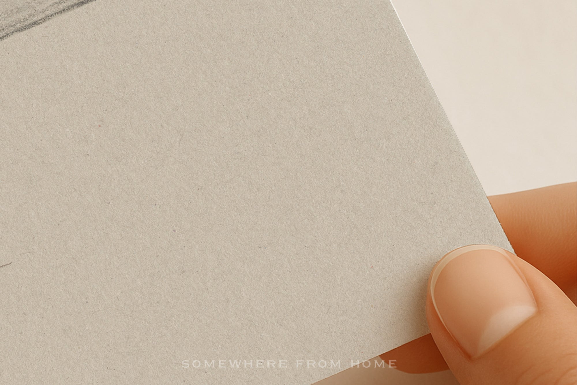 A close-up of a hand holding a textured, light warm gray or beige paper sheet against a clean off-white background.