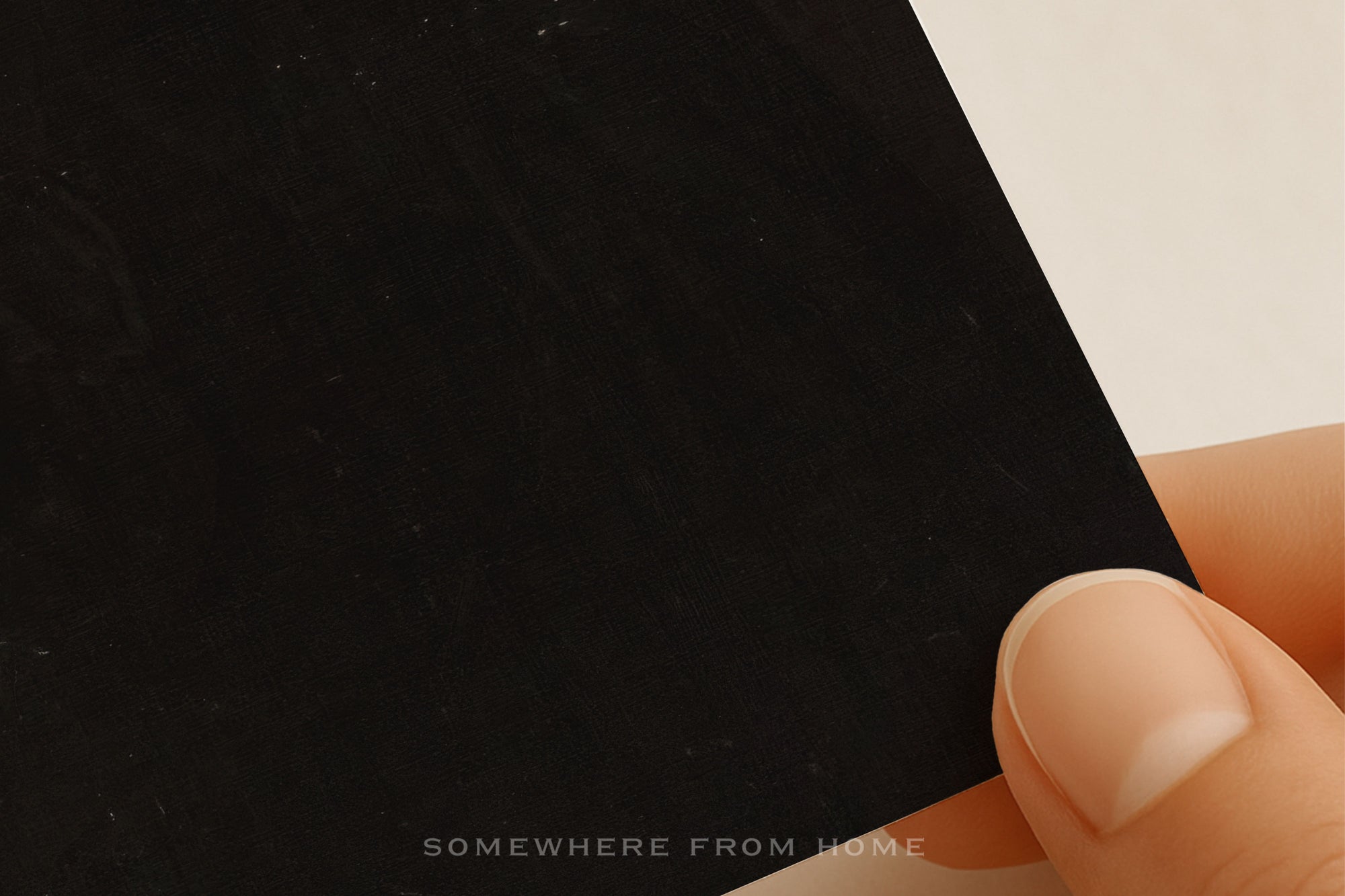 Hand holding a black card with 'SOMewhere from home' text on a light background